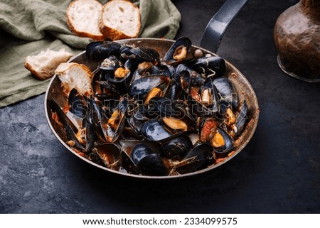 Traditional barbecue Italian blue mussel in tomato red wine sauce with baguette bread as close-up in a rustic iron pan Royalty-Free Stock Photo #2334099575