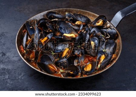 Traditional barbecue Italian blue mussel in tomato red wine sauce with herb and garlic as close-up in a rustic iron pan Royalty-Free Stock Photo #2334099623