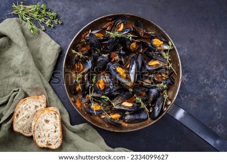 Traditional barbecue Italian blue mussel in tomato red wine sauce with baguette bread as top view in a rustic iron pan  Royalty-Free Stock Photo #2334099627