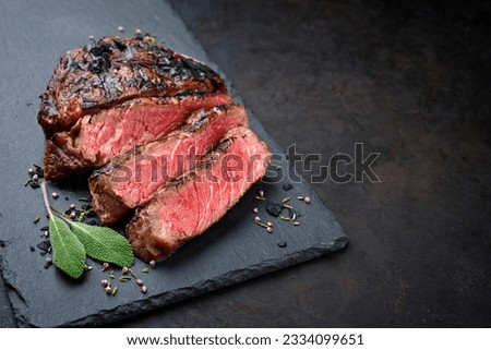 Barbecue dry aged wagyu rib-eye beef steaks with herb and black salt served as close-up on a black board with copy space right Royalty-Free Stock Photo #2334099651