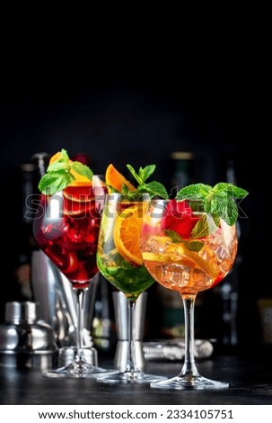 Red, white, rose sangria summer alcoholic cocktail drinks with spanish wine, fruits, citrus and ice. Black bar counter background, steel bar tools and bottles Royalty-Free Stock Photo #2334105751