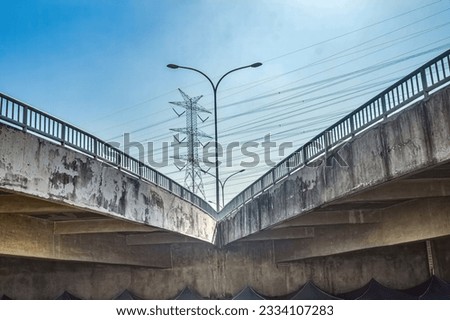 branching of a pedestrian bridge or flyover bridge with a street lighting pole in the middle against a backdrop of high-voltage power towers and a clear blue sky during hot weather Royalty-Free Stock Photo #2334107283