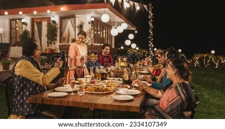 Big Family Celebrating Diwali: Indian Family in Traditional Clothes Gathered Together on a Dinner Table in a Backyard Garden Full of Lights. Moment of Happiness on a Hindu Holiday Royalty-Free Stock Photo #2334107349