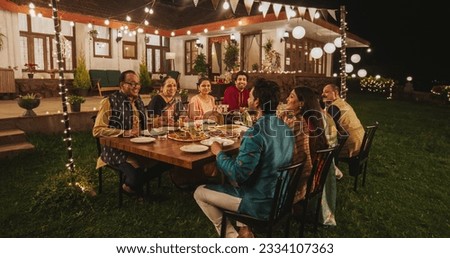 Big Indian Family Celebrating Diwali: Family Gathered Together on a Dinner Table in a Backyard Garden Full of Lights. Group of Adults Sharing Food, Laughs and Stories on a Hindu Holiday Royalty-Free Stock Photo #2334107363