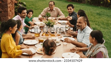 Indian Family Gathering Portrait: Family and Friends Celebrating Outside at Home. Diverse Group of Children, Adults and Seniors Sitting at a Table, Having Fun Conversations. Eating Traditional Food