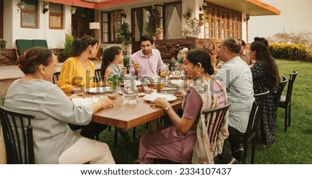 Indian Family Gathering Portrait: Family and Friends Celebrating Outside at Home. Diverse Group of Children, Adults and Seniors Sitting at a Table, Having Fun Conversations. Eating Traditional Food