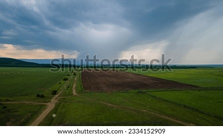 Aerial view of the meadows with cows and horses near to the mountain ridge and country road at summer cloud rain day, blue color of the picture