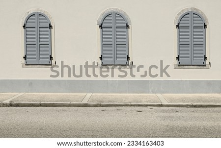 Closed gray arched shutters on a white facade. Concrete sidewalk and street in front. Background for copy space.