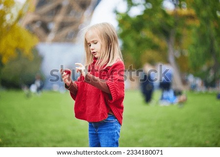 Adorable preschooler girl eating strawberry near the Eiffel tower in Paris, France. Happy child playing with toys in park on a fall day. Kid enjoying healthy snacks outdoors