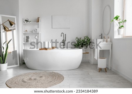 Interior of light bathroom with bathtub, shelving unit and dressing table Royalty-Free Stock Photo #2334184389