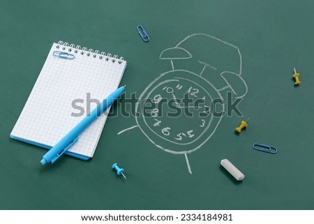 Blank notebook with stationery and drawn alarm clock on green chalkboard