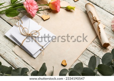 Composition with blank card, envelopes, eucalyptus branch and beautiful eustoma flowers on light wooden background, closeup
