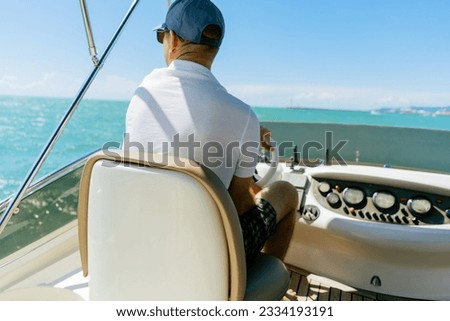 Bach view of middle-aged man driving luxury motor yacht. Captain at the helm of motor boat. Image with selective focus Royalty-Free Stock Photo #2334193191