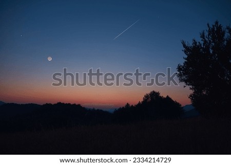 Silhouette of a countryside with Milky Way stars, shooting star, planets and crescent Moon.