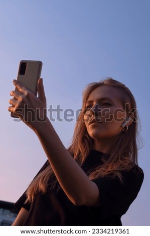beautiful girl in headphones holds a phone in front of her against the sunset sky
