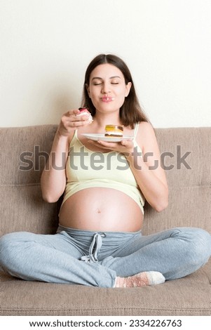Young pregnant woman enjoys eating tasty cake resting on the sofa at home. Unhealthy diet during pregnancy concept.