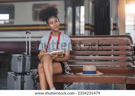Asian African female tourist traveler holding mobile phone smart phone sitting at train station, Confident smiling teenager girl playing smart phone laptop computer on suit case at station