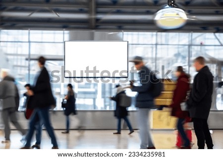 Interactive signage TV screen display at airport or metro transportation station with blurred busy people moving around