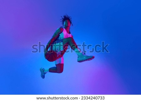 Slam dunk Ambitious young man, basketball player in minions, playing basketball against gradient blue background in neon lights. Concept of professional sport, competition, hobby, competition, ad