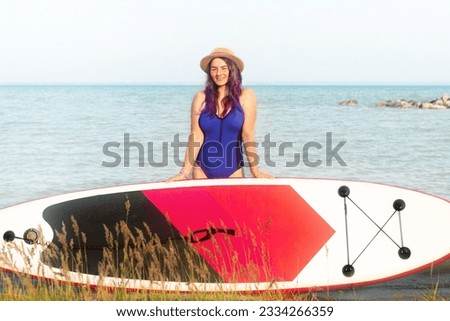 Sup boarding. A woman in a hat poses standing with a sup board. The concept of active lifestyle and surfing.