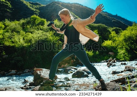 Young woman hiker crossing mountain stream at sunny day