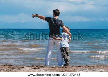 Father and son hugging on the shore of the lake and looking away Royalty-Free Stock Photo #2334272463