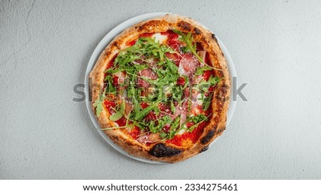 A top view of a pizza with arugula and prosciutto on a table