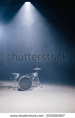 A drum set against a black background. A spotlight illuminates the drum from above. A fog machine makes fog. There is space for text.