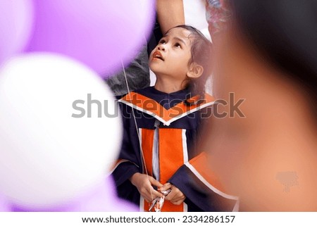Portrait of cute Asian girl with graduation gown in school who is interested in transparent balls                              