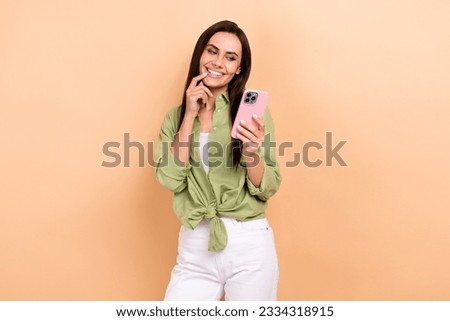 Photo of minded positive nice person finger touch lips use smart phone blogging isolated on beige color background