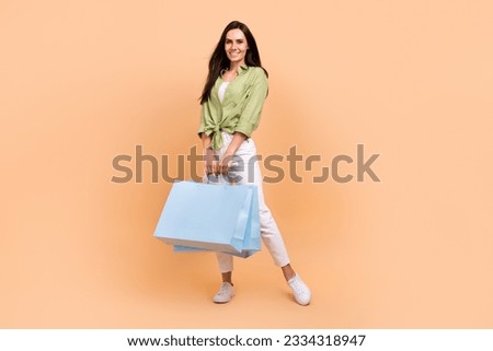 Full size photo of nice cute adorable girl dressed green blouse white trousers hold new clothes bags isolated on beige color background