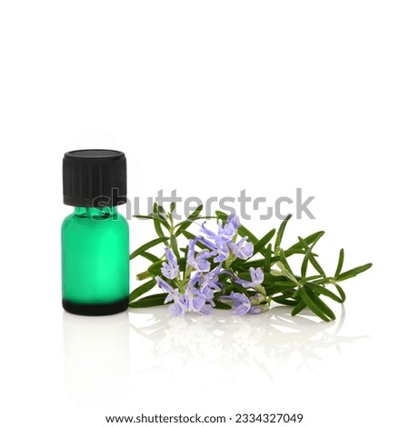 Rosemary herb leaf sprig in flower with a green aromatherapy essential oil bottle, over white background.