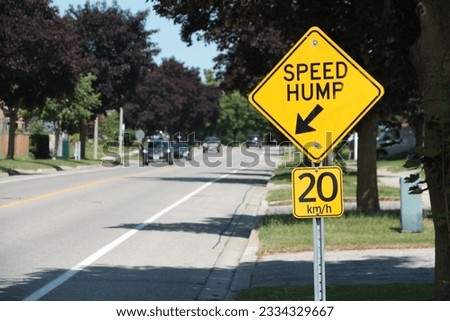 close on speed hump arrow 20 km h sign in black writing on yellow background silver post and blurred cars approaching in background