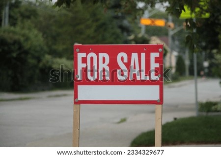 generic for sale sign on front lawn of residential home in white writing on red background and wood posts with blurred long street behind - close shot center right frame
