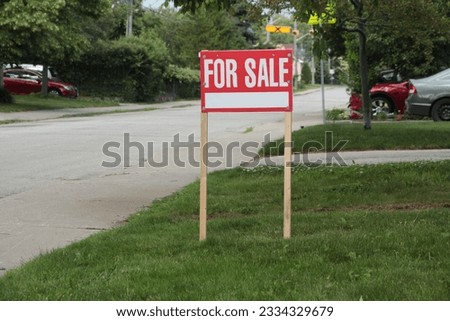generic for sale sign on front lawn of residential home in white writing on red background and wood posts with blurred long street behind - medium shot center right frame
