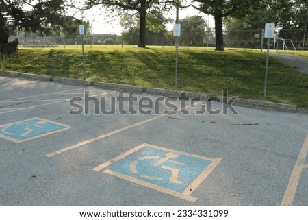 two handicap parking spots with blue and yellow handicap logo inside them, shot from side angle, small grass hill and soccer field behind them