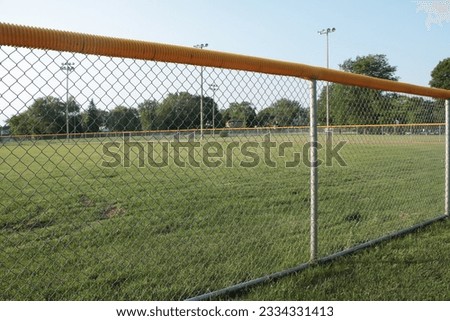medium wide shot of non professional baseball outfield shot through foul line fence with yellow top and soccer field trees lights and sky in the background