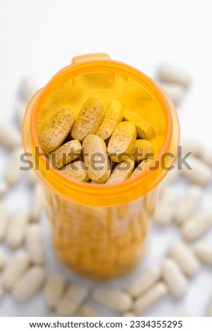 High angle view of a yellow pill bottle full of tablets. Tablets are also scattered around on a white surface. Vertical shot.