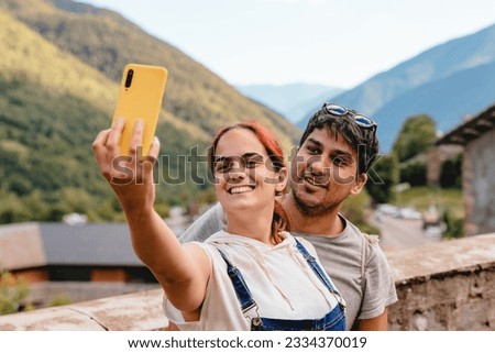 Couple taking a selfie with phone while doing rural tourism in a mountain village. Holiday trip and outdoor summer vacation in Huesca, Spain