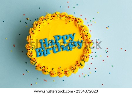 Yellow birthday cake with blue happy birthday greeting and sugar sprinkles against a blue background