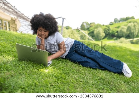 Little girl using laptop in summer garden video call watching movie online lesson distance education.