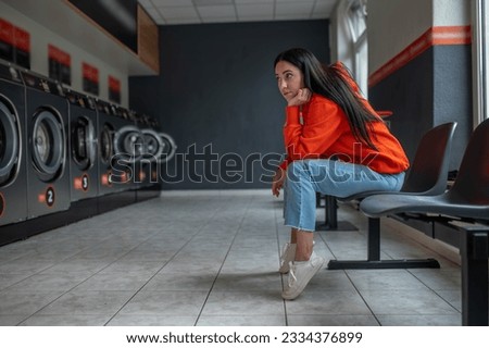 Tired bored woman sitting in automatic laundry room while waiting for the laundry to be done. Royalty-Free Stock Photo #2334376899