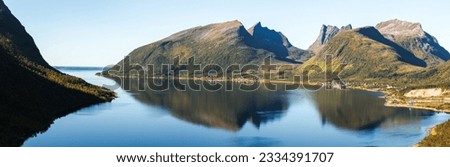 Serene mountain lake nestled amidst towering green mountains.Crystal-clear deep blue water reflects clear blue sky adorned with fluffy clouds.This tranquil scene showcases untouched beauty of nature. Royalty-Free Stock Photo #2334391707