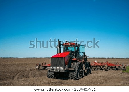 A large farm tractor with planting equipment in a large grain field in spring.