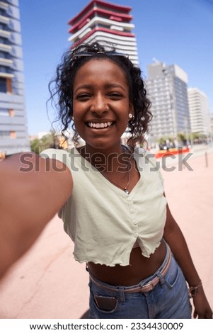 Vertical young African American girl taking a smiling selfie. Happy beautiful woman posing for photo in the city in summer. Cheerful people on vacation enjoying their outdoor. Weekend getaway person. Royalty-Free Stock Photo #2334430009