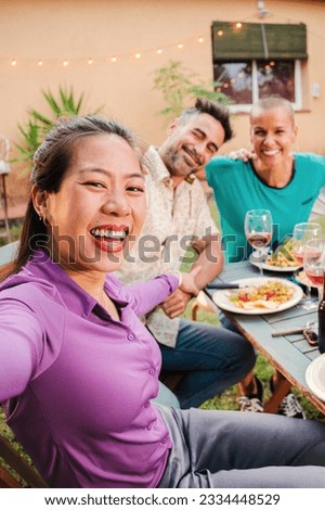 Vertical portrait of a group of mature adult best friends smiling taking a selfie on a barbeque party celebration at home backyard. Middle age happy people shooting pictures sitting at patio table