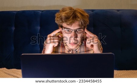 A young student with glasses is working on a laptop looking at the screen.
