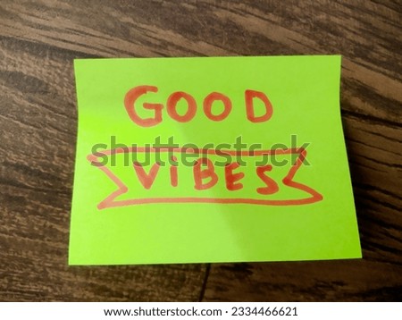Message written with the word "Good Vibes" on yellow paper, written in English in pink letters, on a wooden background.