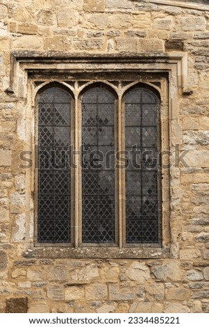Realistic photo of British triple lancet window on medieval stone wall. Metal grill, deep recess, large stone blocks, stone casing. Gothic architecture, historical detail.