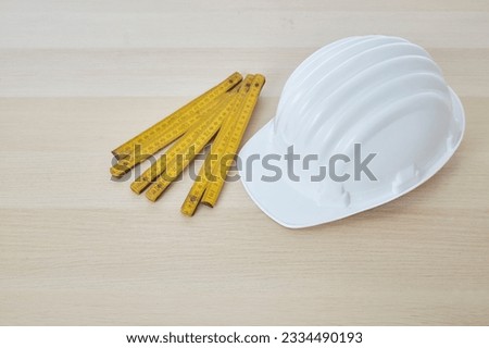 Construction tools and a white hard hat with a measuring stick, paper house building plan on a wooden work table copy space for text Royalty-Free Stock Photo #2334490193